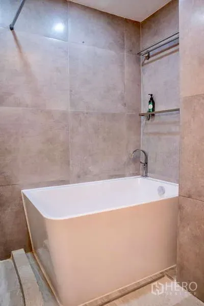 Townhouse for rent in Khlong Toei, Bangkok - Deep soaking bathtub against tiled walls with a shelf above.