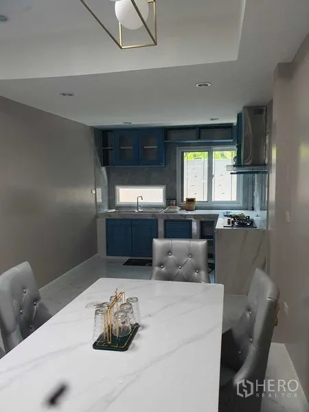 Home Office for rent in Suan Luang, Bangkok - Dining area with a marble table beside a blue built-in kitchen.