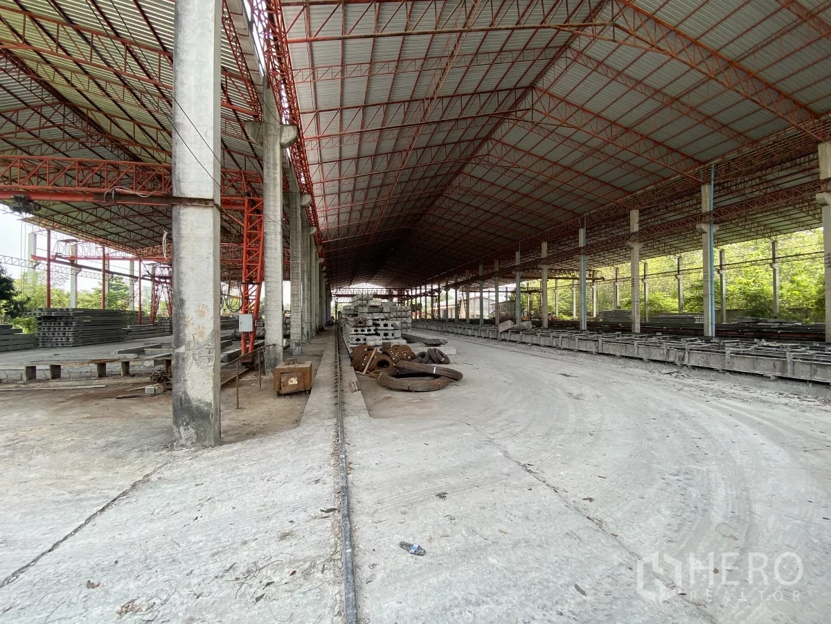Factory for sale in Chon Buri - Wide covered lanes and rail tracks inside a vast steel-framed factory hall.