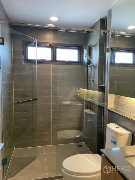 Detached House for rent in Bang Kapi, Bangkok - Guest bathroom with large mirror, glass shower enclosure and grey tiles.