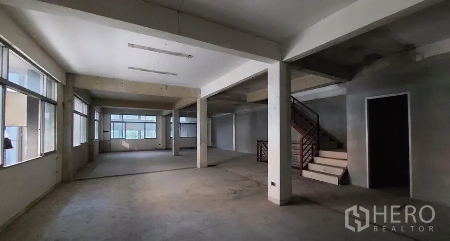 Shophouse for rent in Watthana, Bangkok - Open-plan shophouse interior in Ekkamai, Bangkok with large windows, concrete floors, support columns and an internal staircase.
