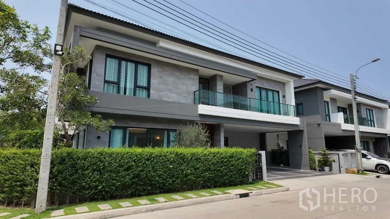 独立式住宅 出租或出售在Bang Na, Bangkok - 现代两层独栋别墅外观，玻璃阳台与绿篱前庭，位于曼谷邦纳。