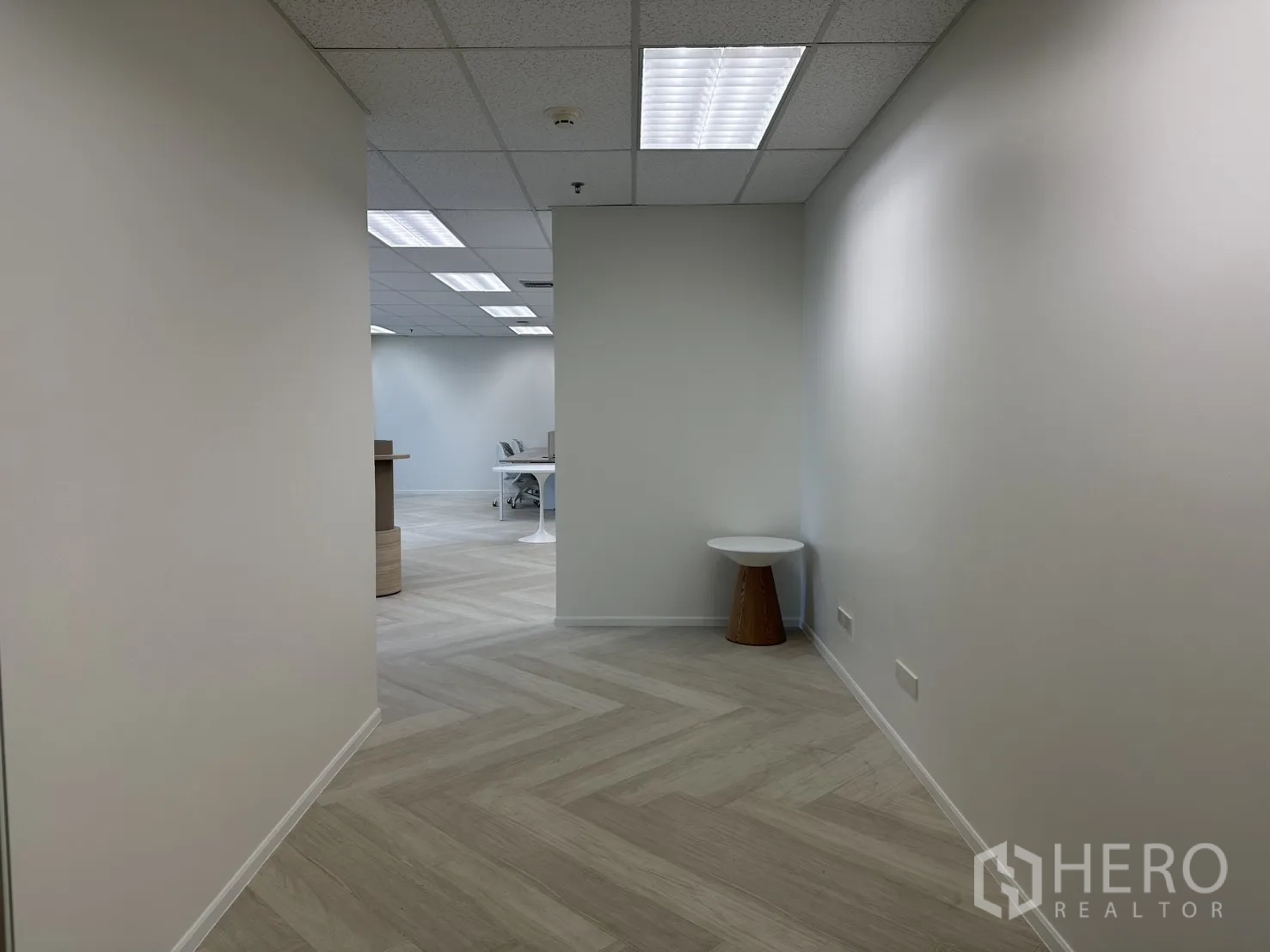 Office Space for rent in Sathon, Bangkok - Entry corridor to an open-plan office with herringbone flooring, grid ceiling lights, and a small side table.