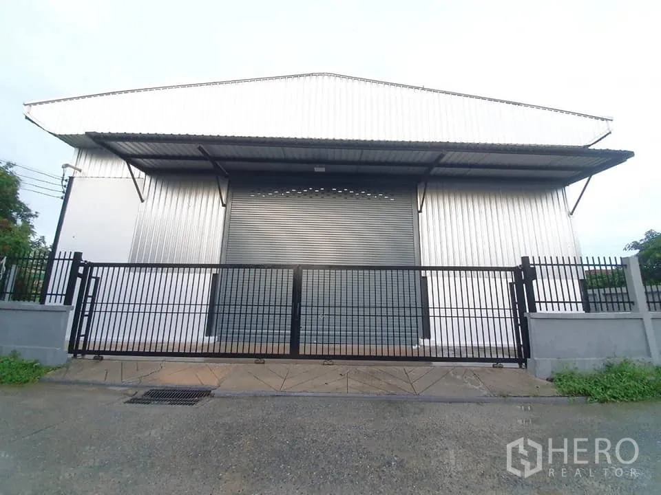 Warehouse for rent in Bang Khen, Bangkok - Front view of the warehouse with closed roller shutter and black sliding gate along the street.