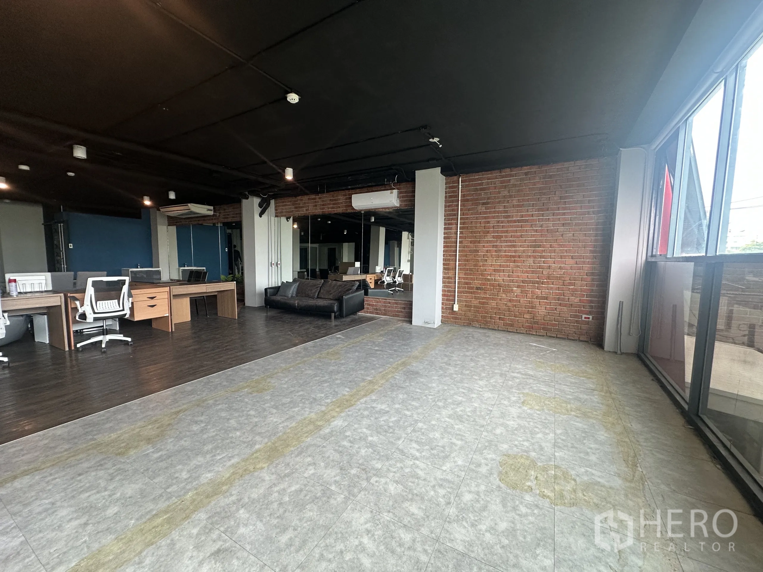Office Space for rent in Watthana, Bangkok - Corner workspace with large windows, brick feature wall and tiled floor beside workstations.