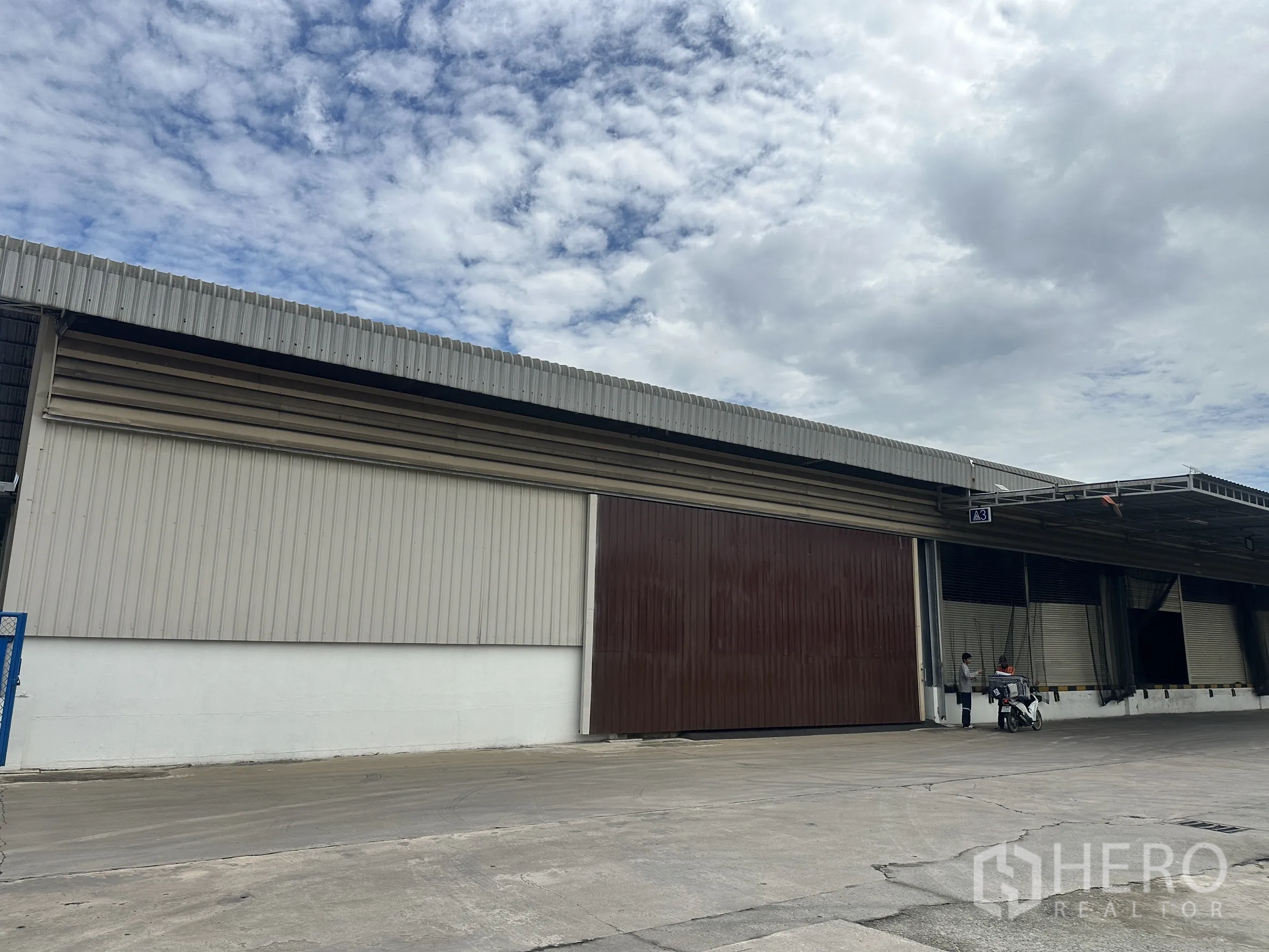 Factory for rent in Lat Krabang, Bangkok - Side view of metal-clad factory with a large brown sliding door and canopy.