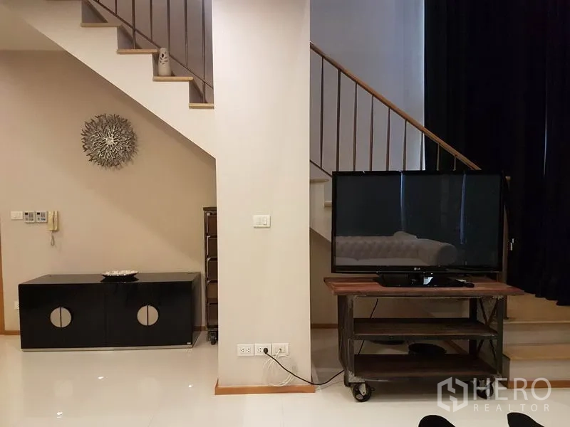 Condominium for rent or sale in Khlong Toei, Bangkok - TV on a media cart beside the staircase and minimalist console.
