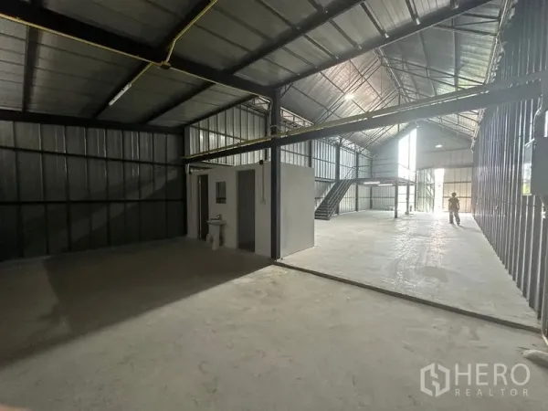 Warehouse for rent in Bueng Kum, Bangkok - Open-plan storage area with a restroom block and natural light from tall front windows.