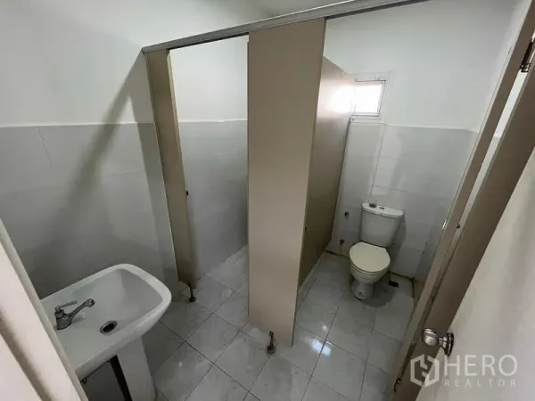 Warehouse for rent or sale in Nonthaburi - Clean restroom with cubicles, sink, and tiled walls and floor.