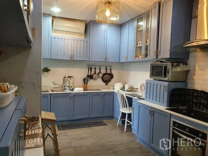 Detached House for sale in Lam Luk Ka, Pathum Thani - Contemporary kitchen with blue cabinetry, white subway tiles, gas hob, range hood and pendant light.