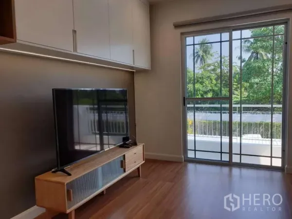 Detached House for rent in Sathon, Bangkok - Cozy living area with TV console and sliding door opening to a balcony facing greenery.