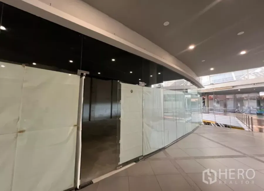 Retail Space for rent - Curved glass storefront of a second-floor retail unit along an indoor mall corridor with ceiling lights.