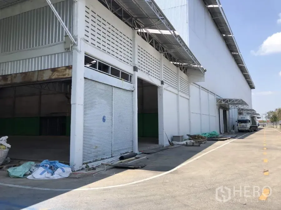 Warehouse for rent in Pathum Thani - Warehouse exterior with multiple roller shutters, covered loading bays, and a wide truck-friendly driveway in Pathum Thani.