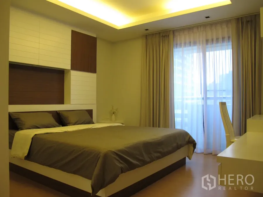 Condominium for rent in Watthana, Bangkok - Warm master bedroom with platform bed, cove lighting and sheer curtains to a balcony.