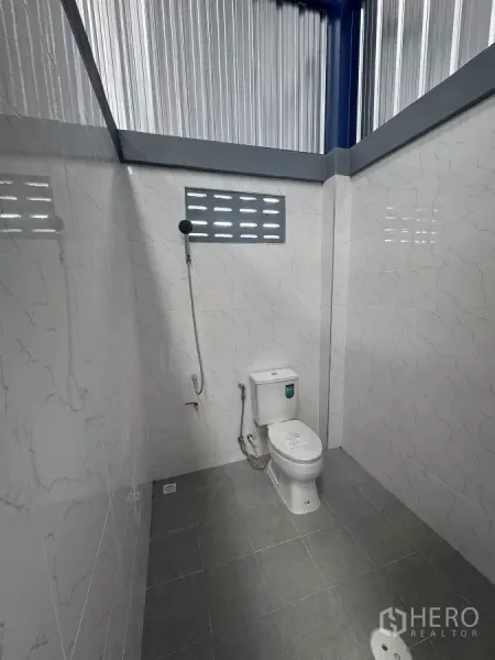 Warehouse for rent in Bang Phli, Samut Prakan - Clean tiled restroom with a flush toilet, handheld bidet spray, and floor drain.