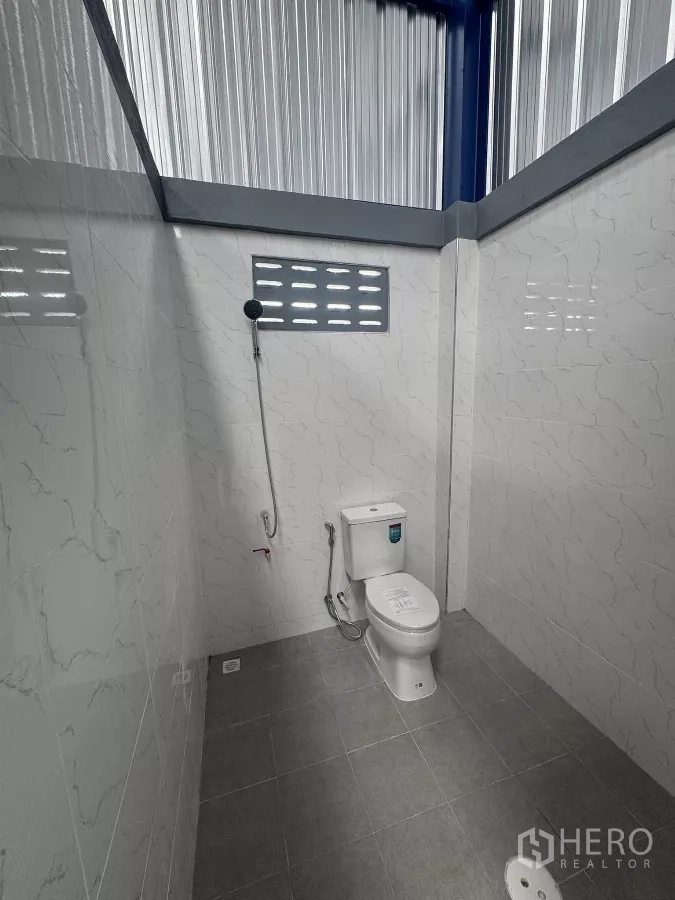 Warehouse for rent in Bang Phli, Samut Prakan - Clean tiled restroom with a flush toilet, handheld bidet spray, and floor drain.