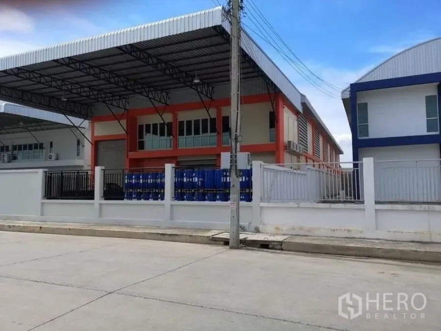 工厂 出租在Samut Prakan - 现代化厂房外观，带棚装卸区、卷帘门及带围栏的前院，临宽阔混凝土路。