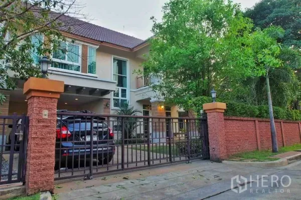 Detached House for rent or sale in Pak Kret, Nonthaburi - Two-storey detached house with gated driveway, carport and mature trees along the fence.