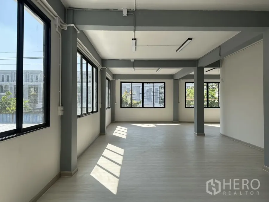 Office Space for rent in Phra Khanong, Bangkok - Sunlit open-plan office floor with large black-framed windows, gray beams, and light vinyl flooring.