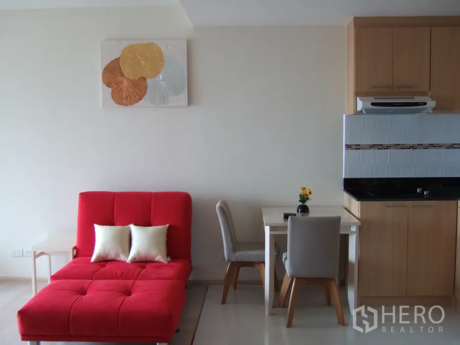 Condominium for rent in Khlong Toei, Bangkok - Bright living area with a bold red chaise sofa, two-seat dining table and compact kitchenette cabinetry.
