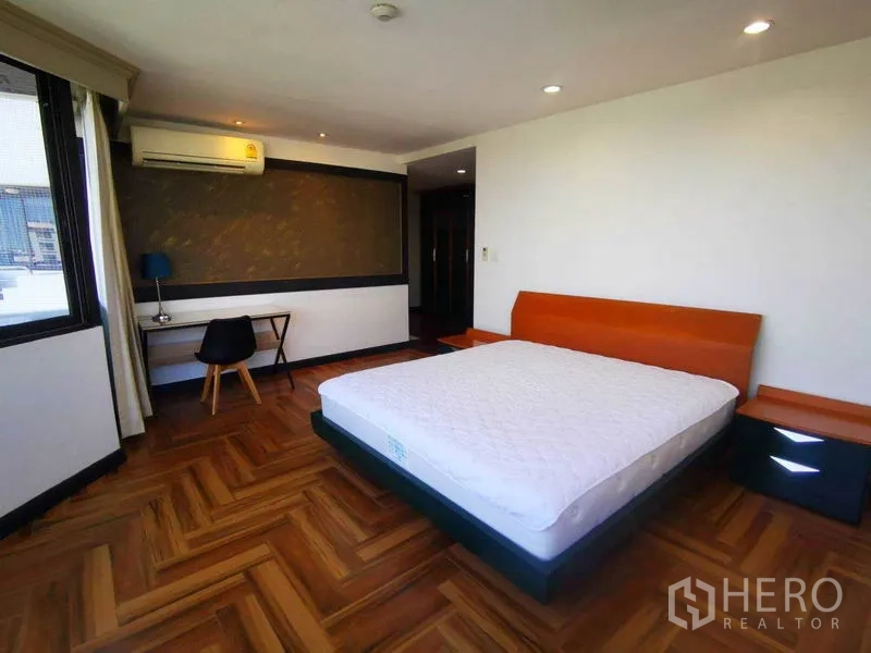 Condominium for rent in Khlong Toei, Bangkok - Spacious bedroom with herringbone wood floor, study desk and wall-mounted air conditioner.