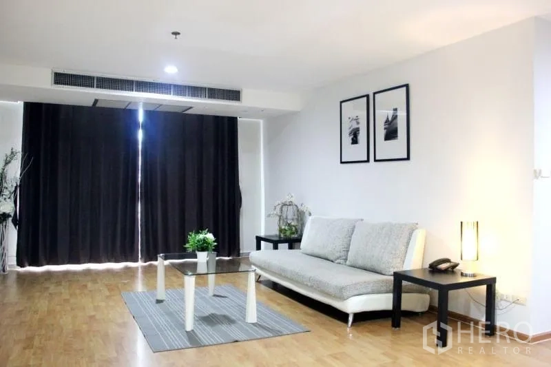 Condominium for rent in Khlong Toei, Bangkok - Spacious living area with blackout curtains, sofa, rug and recessed ceiling lights.