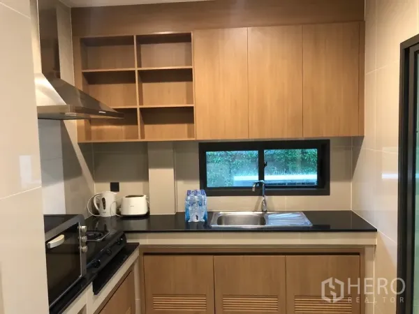 Detached House for rent or sale in Bang Kapi, Bangkok - Separate kitchen with wood cabinets, black countertop, hob, hood and a window for ventilation.