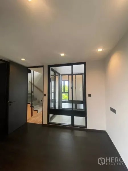 Townhouse for rent in Huai Khwang, Bangkok - Room with dark flooring and a glass partition looking toward the staircase.
