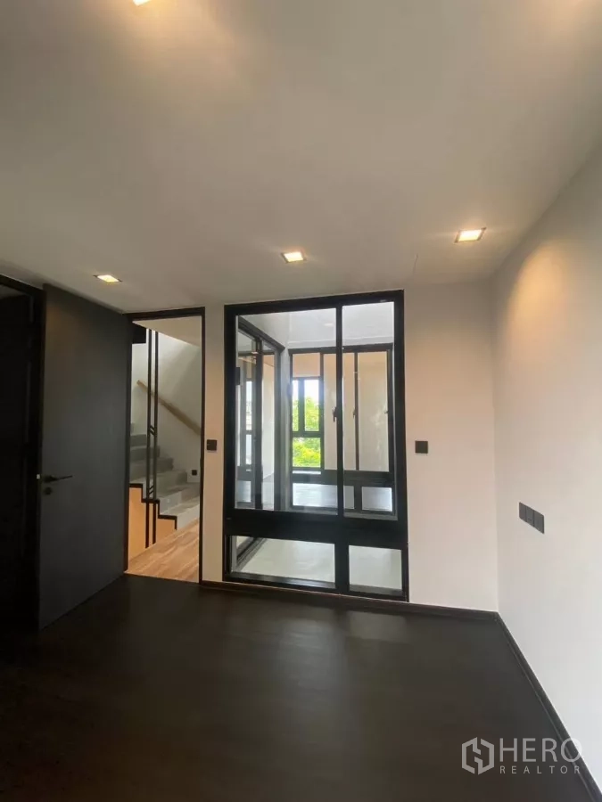 Townhouse for rent in Huai Khwang, Bangkok - Room with dark flooring and a glass partition looking toward the staircase.