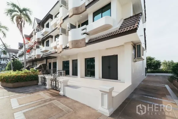 Townhouse for rent in Watthana, Bangkok - Side view of white townhouse row with landscaped walkway and balconies near Phra Khanong.