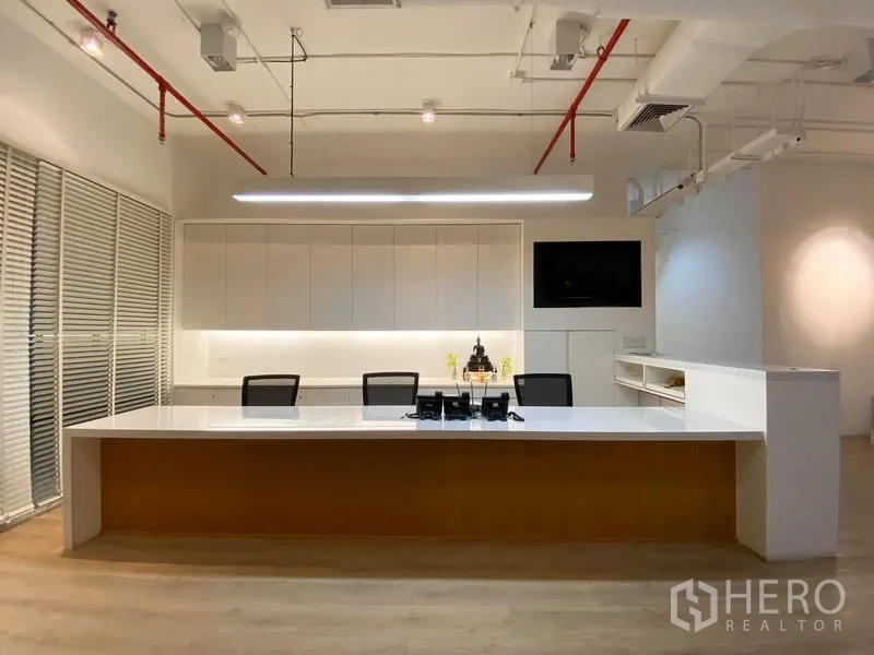 Office Space for rent in Bangkok - Reception with a long white counter, built-in cabinets, wall-mounted screen and exposed ceiling services.