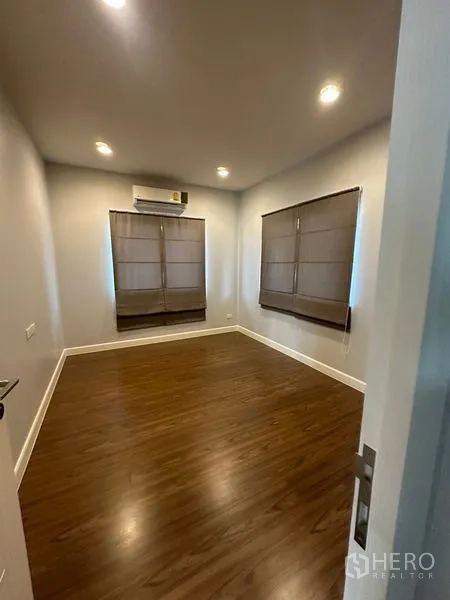 Detached House for rent or sale in Lam Luk Ka, Pathum Thani - Empty bedroom with wood floors, window blinds and a wall-mounted air conditioner.
