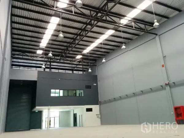 Factory for rent in Samut Prakan - Warehouse hall with mezzanine office block, high ceiling, and large roller shutter door.
