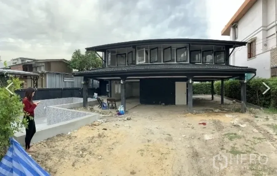 Detached House for sale in Suan Luang, Bangkok - Two-storey black detached house in Suan Luang with raised carport, large front yard and a pool shell under construction.