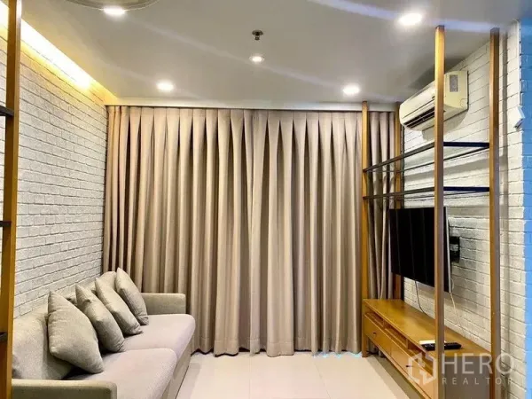 Condominium for rent in Chatuchak, Bangkok - Cozy living room with white brick feature wall, gray sofa, TV unit, and full-length curtains.
