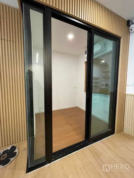 Townhouse for rent or sale in Bang Kapi, Bangkok - Black-framed sliding glass door leading to an enclosed room with wood floor.