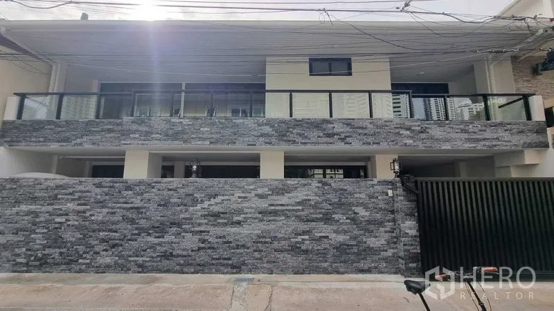 Townhouse for rent in Khlong Toei, Bangkok - Wide exterior view of the townhouse showing stone wall and glass-balustrade balcony.