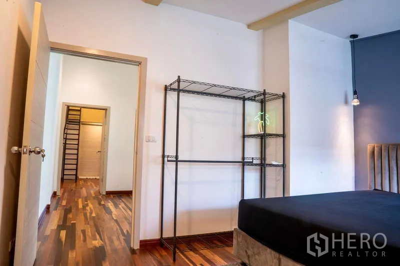 Townhouse for rent in Khlong Toei, Bangkok - Bedroom view toward hallway with wood floors and open wardrobe shelving.