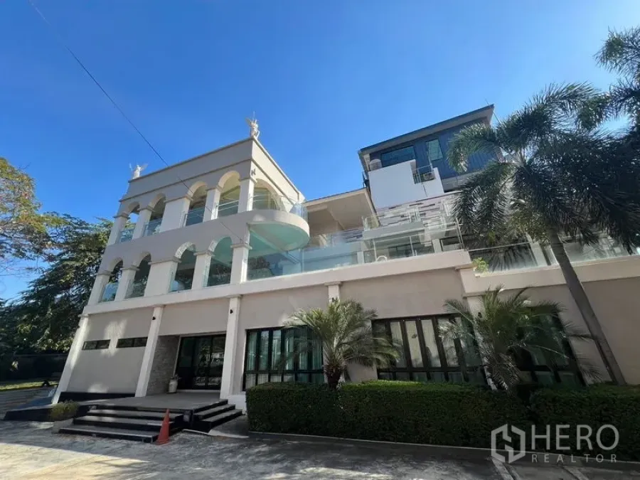 Shophouse for rent in Suan Luang, Bangkok - Grand shophouse exterior with arches, glass balconies and palm landscaping under a blue sky.