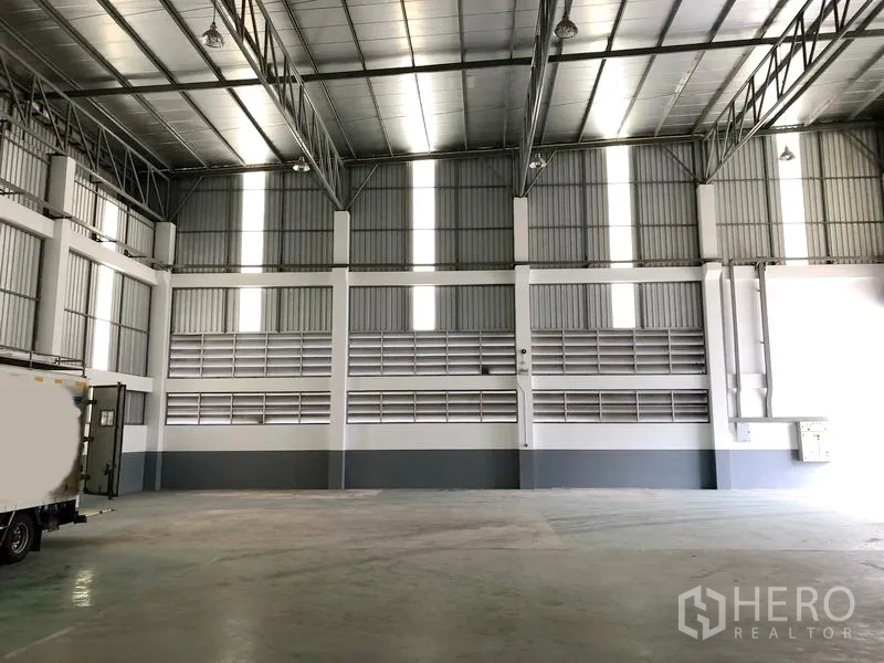 Factory for rent or sale in Samut Prakan - High-clearance warehouse interior with steel truss roof, skylights and polished concrete floor.