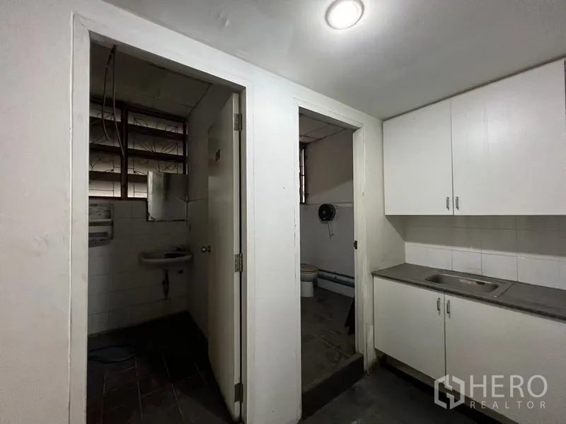 Warehouse for rent in Suan Luang, Bangkok - Utility corner with kitchenette cabinetry, sink, and two separate restrooms inside the warehouse.