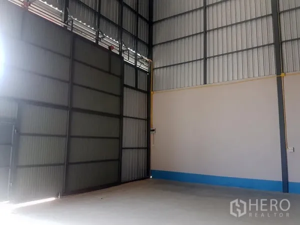 Warehouse for rent in Prawet, Bangkok - Interior of a high-ceiling warehouse with corrugated steel walls, large sliding door and concrete floor.