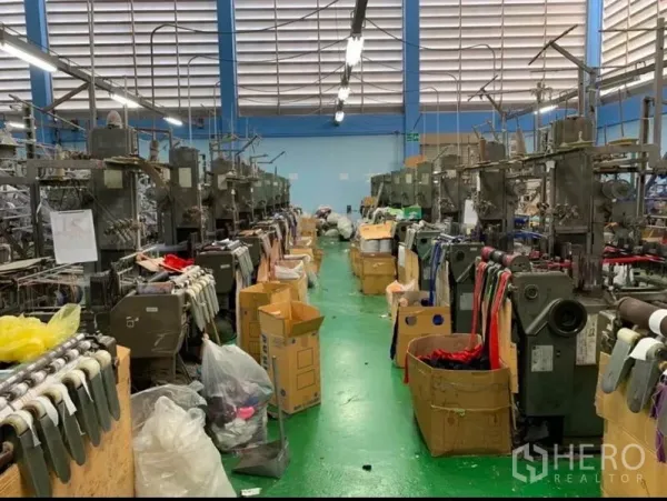 Warehouse for sale in Mueang Samut Sakhon, Samut Sakhon - Aisle between rows of textile machines on a green factory floor under bright lighting.