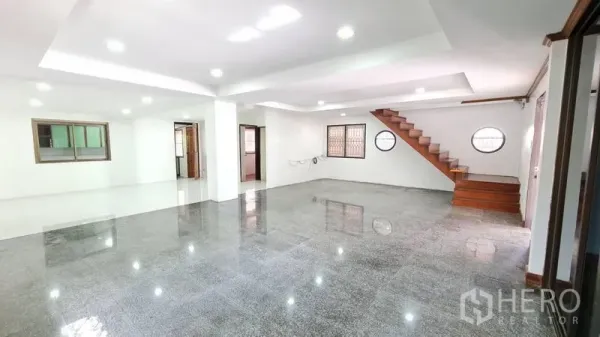 Detached House for rent in Lat Phrao, Bangkok - Spacious living room view showing staircase, large windows and glossy floor tiles.