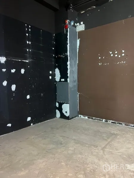 Retail Space for rent in Watthana, Bangkok - Unfurnished shop corner with dark feature walls, patch repairs, exposed utilities, and a concrete floor.