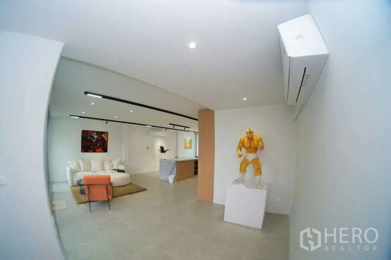 Home Office for rent in Phra Khanong, Bangkok - Spacious lounge in minimalist white with sofa, artwork, modern lighting and a display pedestal.