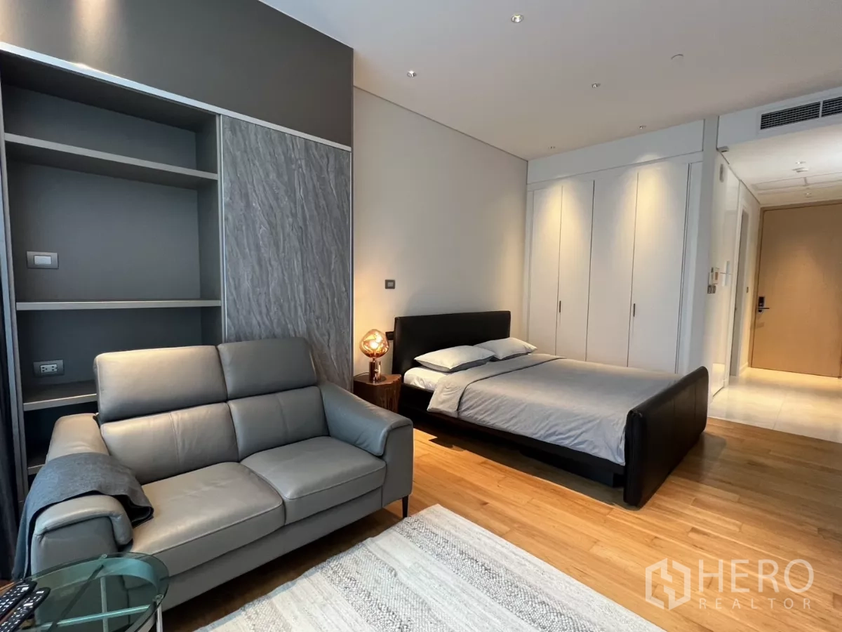 Condominium for rent in Pathum Wan, Bangkok - Open-plan studio with queen bed, grey sofa, warm wood flooring and full-height wardrobes.