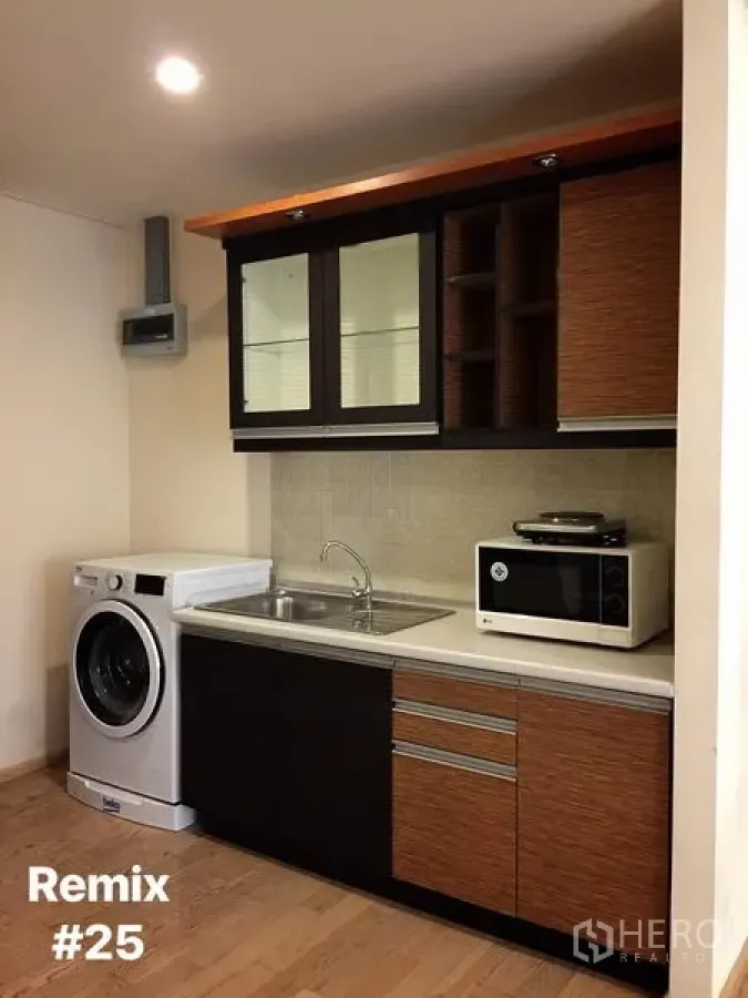 Condominium for rent in Khlong Toei, Bangkok - Compact kitchenette with glass-front cabinets, sink, washing machine, microwave and wood cabinetry in a Bangkok condo.