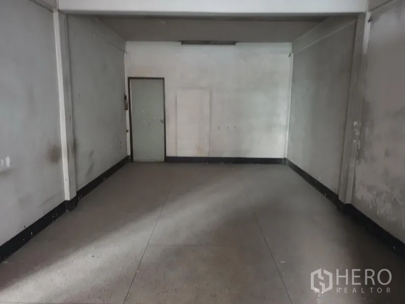 Shophouse for rent in Phra Khanong, Bangkok - Wide vacant room with white walls and a single side door, ready for fit‑out.