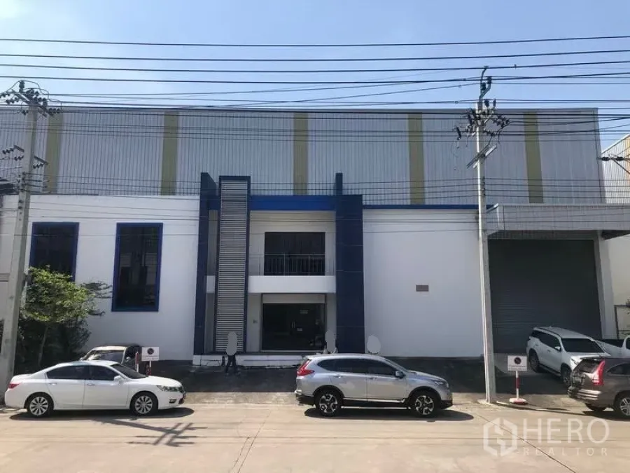 Factory for rent or sale in Bang Phli, Samut Prakan - Modern factory exterior in Bang Phli with parking bays and a large roller shutter entrance.